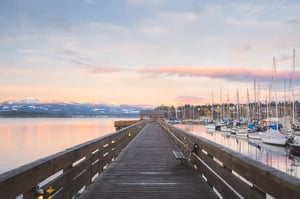 Wooden pier and marina at sunrise with snow-capped mountains across the water