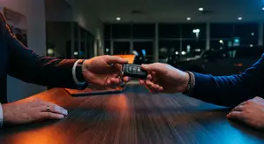 Car keys handed across a desk in a dealership showroom at night